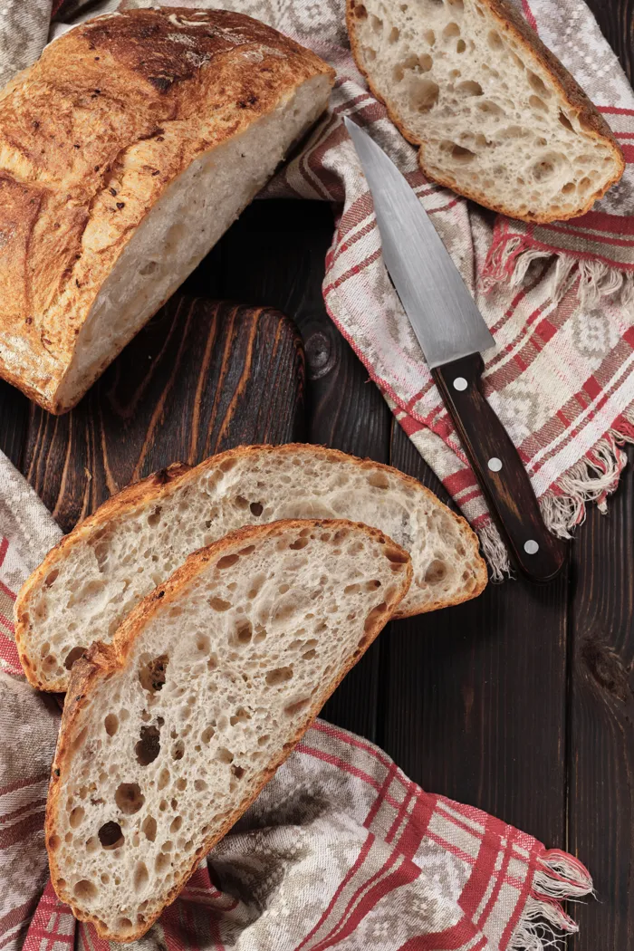 Pagnotta rustica tagliata a fette su un tagliere, con un coltello e un canovaccio